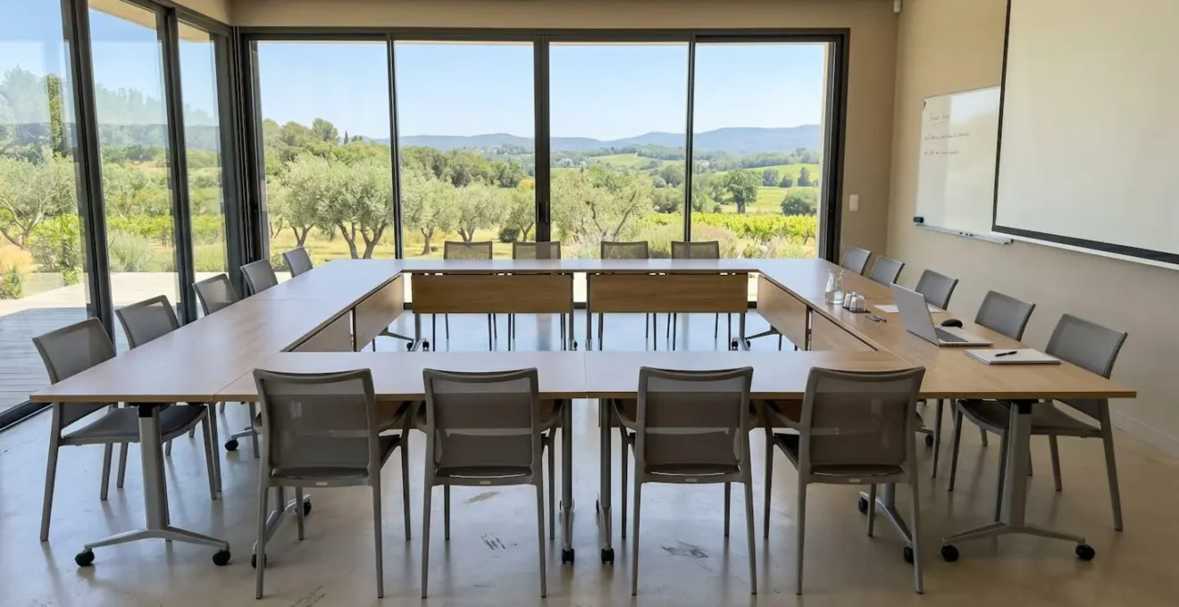 Salle de séminaire contemporaine vide avec tables disposées en U et large baie vitrée donnant sur un jardin méditerranéen